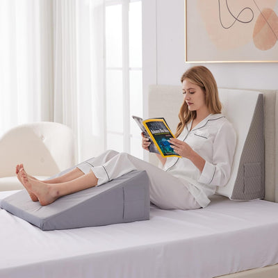 Woman reading in bed using a gray Bed Wedge Pillow to support her legs and back comfortably