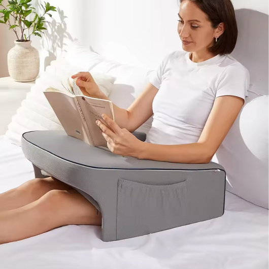 Woman reading book comfortably using a gray Dock Support Cushion on bed
