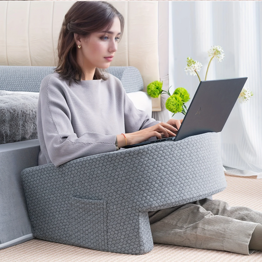 Woman using a gray Lap Reading Pillow while working on a laptop on the floor by the bed